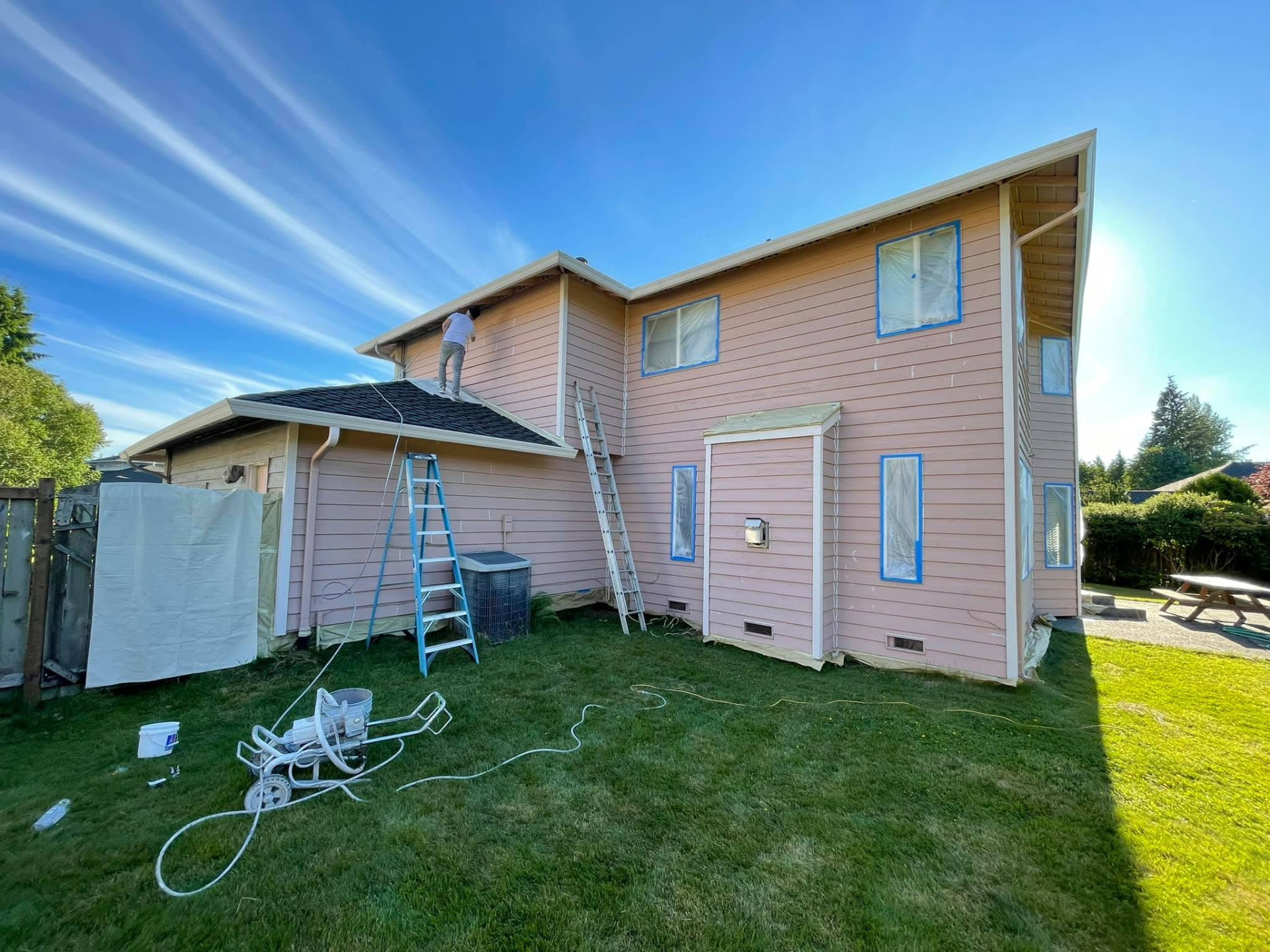 Rear elevation of the same home during prep, lap siding primed and windows taped and plastic-masked